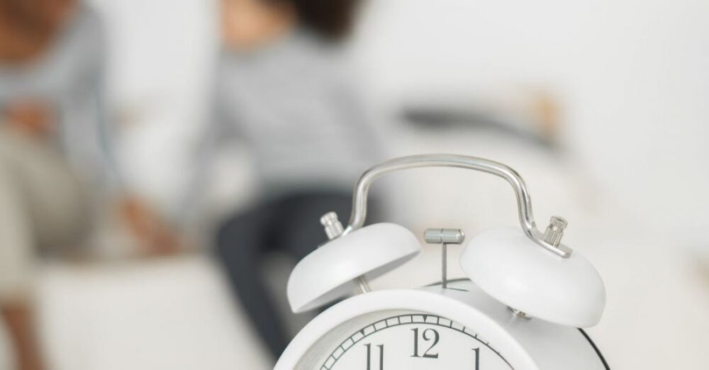 Early Childhood - Retro styled alarm clock placed on table in bedroom near unrecognizable African American little child playing with mother