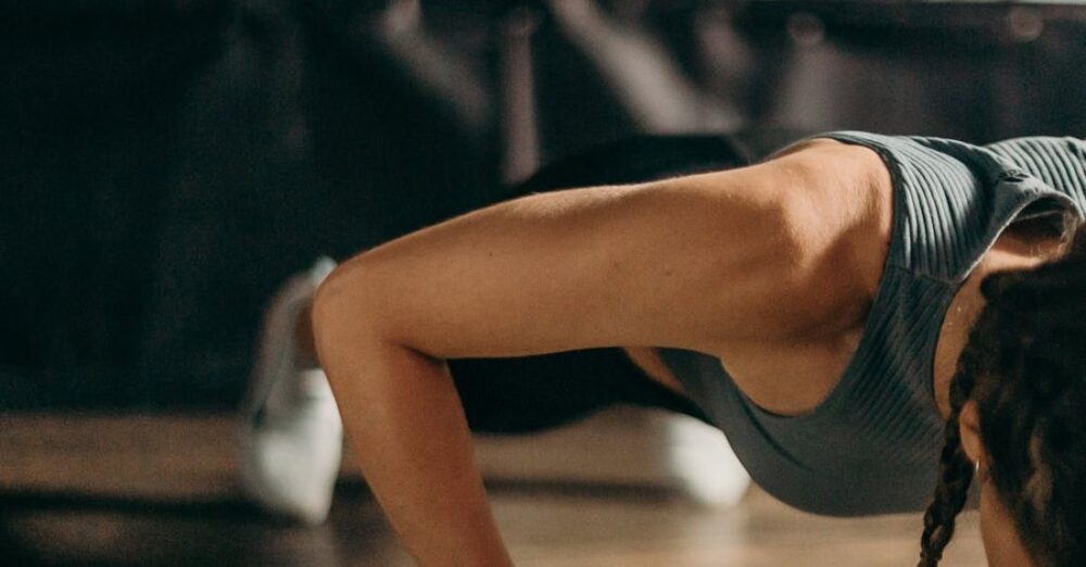 Women's Sports - Woman in Black and White Tank Top and Black Shorts Lying on Brown Wooden Floor