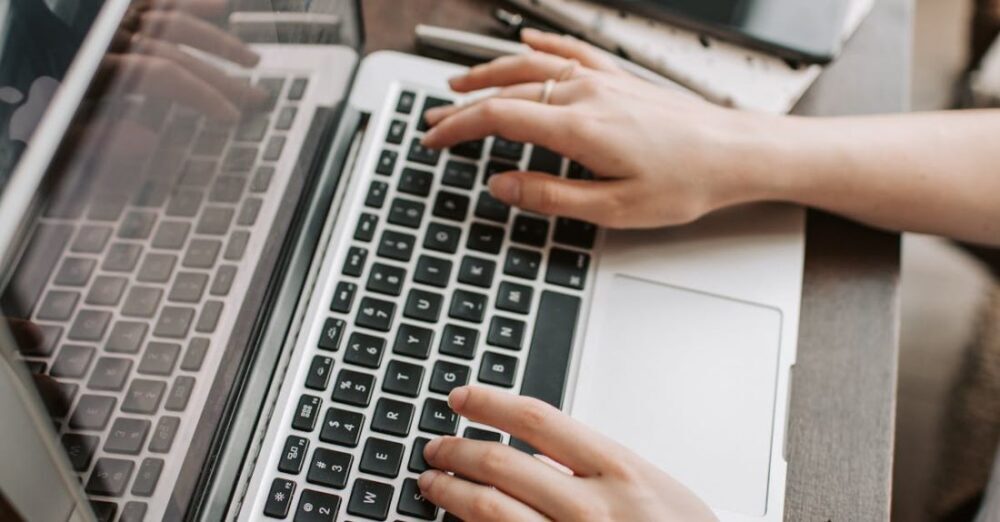 Independent Filmmaking - From above of unrecognizable woman sitting at table and typing on keyboard of computer during remote work in modern workspace