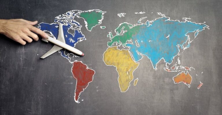 Globalization - Top view of crop anonymous person holding toy airplane on colorful world map drawn on chalkboard